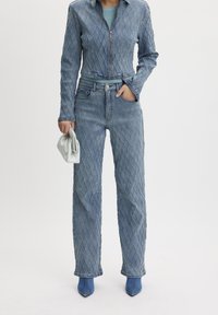 Chaqueta de mezclilla azul acolchada y jeans de tiro alto a juego, con un diseño ajustado y cierre de cremallera. Combinados con un bolso de mano ligero y tacones azules.