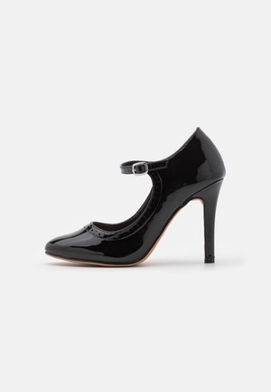 Chaussure à talon haut Mary Jane en cuir verni noir avec un bout rond, une bride de cheville avec boucle en argent et un talon stiletto fin sur fond blanc.