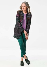 Gebreide cardigan in het zwart met multicolore patronen, met een contrasterende rand. Gecombineerd met een paarse top en teal groene broek. Zwarte instappers.