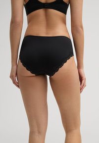 Les culottes en coton noir taille haute présentent une bordure en dentelle festonnée le long des bords, avec une texture lisse et un design minimaliste.