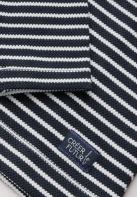 Navy- und weiße gestreifte Stoff mit strukturiertem Gewebe. Enthält ein genähtes Etikett mit der Aufschrift "CREER LE FUTUR" in blauer Stickerei.