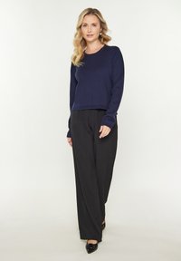 Pulover tricotat bleumarin cu mâneci lungi, decolteu rotund și tiv cu zimți, asortat cu pantaloni negri cu croi larg și pantofi negri cu vârful ascuțit.