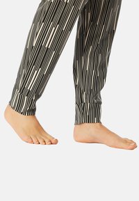 Zwart en crèmekleurige legging met een patroon van verticale strepen, met een strakke enkelontwerp. Een blote voet is zichtbaar aan het einde van het been.