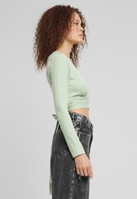 Világoszöld, hosszú ujjú, cropped top, hátsó megkötős részlettel. Fekete, magas derekú farmerral párosítva, amely elhalványult textúrával rendelkezik.