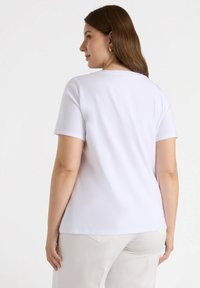 Camiseta blanca de manga corta con cuello redondo, hecha de tela suave. La parte trasera presenta costuras mínimas y un ajuste relajado.