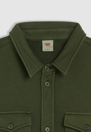 Camicia verde oliva con bottoni, colletto appuntito, due tasche frontali e vestibilità comoda. Tessuto spesso con una texture liscia.