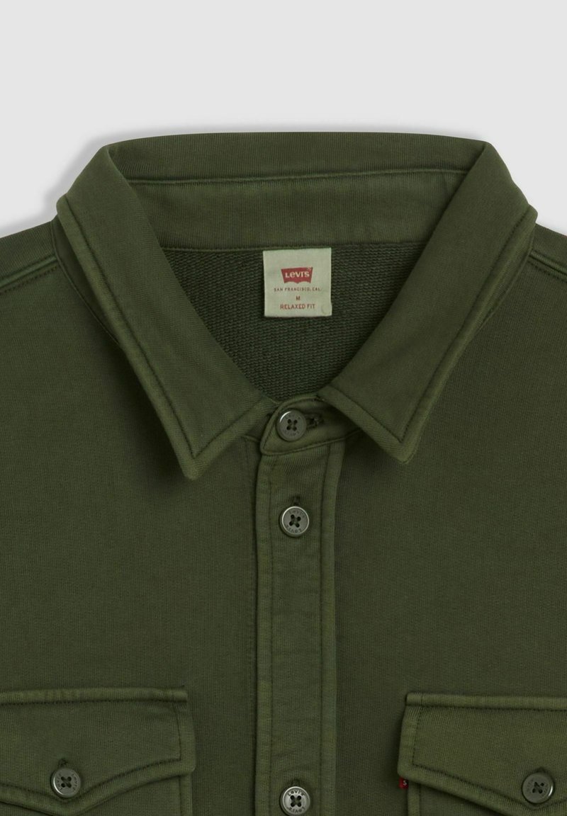Camicia verde oliva con bottoni, colletto appuntito, due tasche frontali e vestibilità comoda. Tessuto spesso con una texture liscia.
