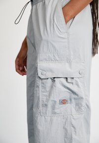 Světle šedé cargo kalhoty vyrobené z texturované tkaniny, s elastickým pasem, bočními kapsami a značkovou nášivkou na noze.