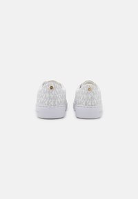 Zapatos deportivos de lona blanca con un patrón texturizado del logo MK, punta redondeada, suela plana blanca y detalle de hardware en tono dorado en la parte trasera.