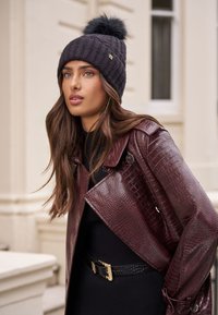 Fekete kötött sapka szőrmés bojt díszítéssel, bordó mű krokodilbőr dzsekihez és arany csatú fekete övhez párosítva.