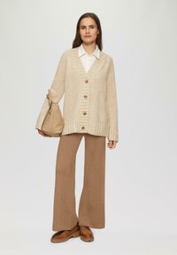 Beige gebreide cardigan met vijf knopen, v-hals, geribbelde manchetten, gecombineerd met bruine wijde broek en bruine enkelboots.