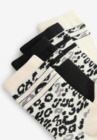 Kolme paria sukkia, joissa on värisekoitus: beige musta- ja harmaa leopardi-kuvio, yksivärinen musta ja mustat valkoisilla raidoilla.
