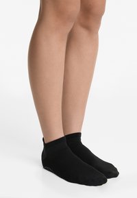 Crne anklets čarape s teksturiranim gornjim dijelom i rebrastim manžetama; imaju točkaste gumene gripove na peti za poboljšano prianjanje.
