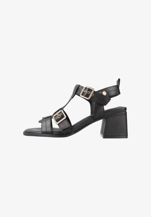 Sandalias de tacón de cuero negro con punta abierta, que presentan dos hebillas ajustables en tono dorado y un diseño de tacón cuadrado. Suela plana, estructura minimalista.