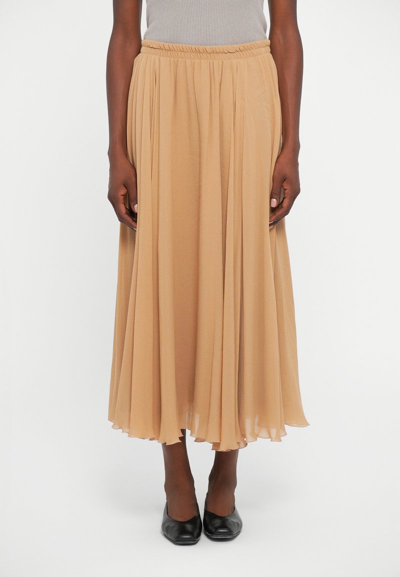 Tan, pleated maxi skirt made of lightweight fabric with an elastic waistband. It falls gracefully to the ankles, enhancing fluidity and movement.