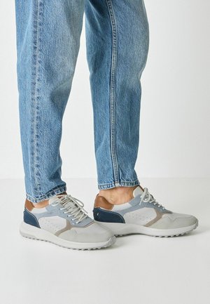 Sive in mornarske superge z usnjenimi in semišasti poudarki, z teksturirano podplatom in luknjastimi oblikovnimi elementi, kombinirane z jeans hlačami.