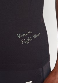 T-shirt noir ajusté en tissu avec le logo "Venum Fight Wear" en lettres vert clair. Texture lisse avec manches courtes et col rond.