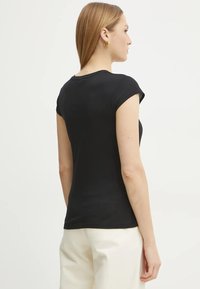 Camiseta negra ajustada de manga corta, con una textura suave y un escote redondeado. El modelo la lleva con pantalones de color claro.