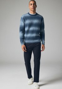 Blau- und grau gestreifter Pullover mit Rundhalsausschnitt und gerippten Bündchen, kombiniert mit dunklen Hosen und weißen Sneakers.