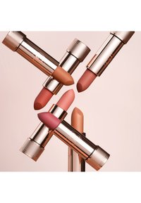Vijf lipsticks in verschillende tinten nude en roze, met metalen roségouden tubes met geribbelde doppen en een gladde matte afwerking.