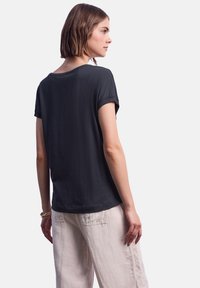 Černé triko s krátkým rukávem, volného střihu, kulatým výstřihem a měkkou texturou, v kombinaci se světlými béžovými lněnými kalhotami.