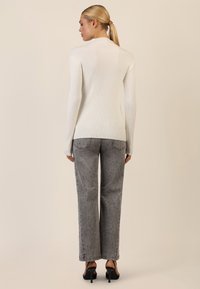Langærmet, ribbet hvid top parret med grå lige ben-jeans med et prikket mønster og sorte højhælede sandaler.