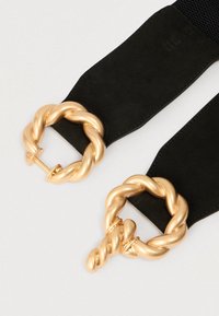 Ceinture élastique noire avec deux boucles en métal doré torsadé ; texture lisse et formes arrondies. Chaque boucle présente un design en boucle.
