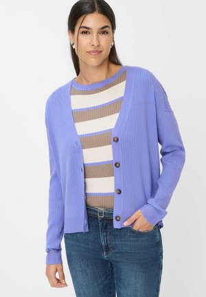 Lavender ribbed cardigan with a relaxed fit, featuring brown buttons, paired with a striped top in beige and blue, worn with dark jeans.