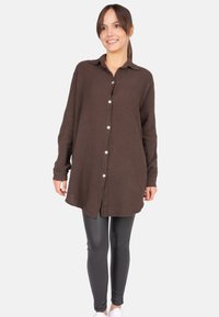 Brown button-up shirt in textured fabric, featuring a collar and long sleeves, paired with shiny black leggings and white sneakers.