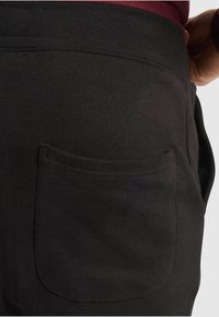 Black sweatpants with a flat waistband, side pocket visible, and smooth texture, designed for comfort and ease of movement.