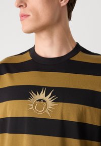 Zwart en gouden gestreept T-shirt met een ronde halslijn. Heeft een centraal geborduurd zonmotief met een glimlachend gezicht.