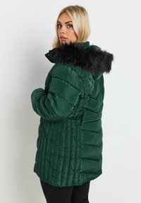 Grön puffjacka med en huva av kunstpäls, quiltat mönster, tvåvägsdragkedjefickor och insvängd midja för en skräddarsydd look.