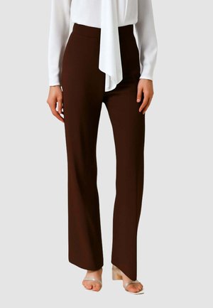 Pantaloni marroni a vita alta, a gamba dritta, con una texture liscia. Abbinati a una camicetta bianca e sandali trasparenti con tacco.