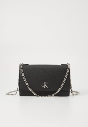 Schwarze Leder-Umhängetasche mit einer silbernen Kettenriemen, die ein umklappbares Design und ein geprägtes "CK"-Logo auf der Vorderseite aufweist.