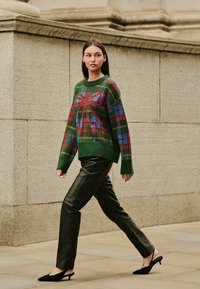 Zelený pletený sveter s farebným kockovaným vzorom a dizajnom mašle, skombinovaný s čiernymi koženými nohavicami a čiernymi slingback podpatkami.