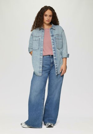 Chemise en denim bleu clair surdimensionnée, t-shirt rose en dessous, jeans bleu à jambes larges, baskets argentées. Texture lisse, coupe décontractée, deux poches avant.