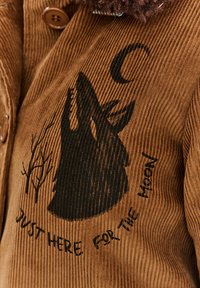 Brązowa kurtka z korduroju z sylwetką czarnego wilka i wzorem drzew, z napisem "Tylko tu dla księżyca" poniżej.