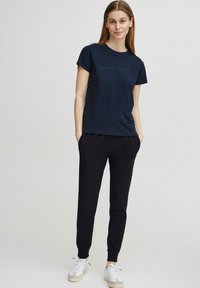Camiseta azul marino con cuello redondo y mangas cortas, combinada con joggers negros y zapatillas blancas, con puños elásticos y bolsillos laterales.