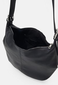 Sac en cuir noir à bandoulière avec un extérieur texturé, une fermeture éclair et un intérieur spacieux avec une poche zippée supplémentaire.