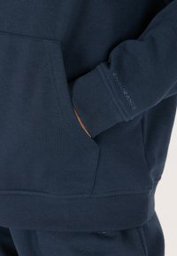 Sudadera azul marino con puños y dobladillo acanalados, que presenta un bolsillo frontal. Logo "ENDURANCE" en la manga en una impresión sutil y contrastante.