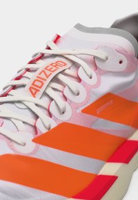 Κοντινό πλάνο λευκού και πορτοκαλί αθλητικού παπουτσιού Adidas Adizero με λευκά κορδόνια και επάνω μέρος από υφασμάτινη υφή.