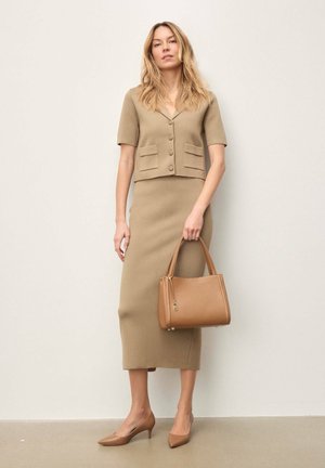 Costum din tricot bej compus din top cu mâneci scurte și nasturi și fustă midi mulată. Însoțit de o geantă maro deschis și pantofi cu vârf ascuțit.