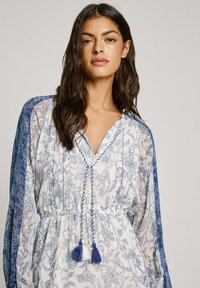 Kleid mit Blumenmuster aus leichtem Stoff, mit tiefem V-Ausschnitt und blauen Akzenten. Verfügt über einen Kordelzug mit Quasten und lange Ärmel.