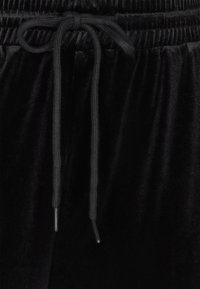 Fekete bársony nadrág elasztikus derékpánttal és húzózsinórral. Puha tapintású, és keskenyített fazonú. Egyszerű, funkcionális stílus.