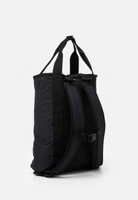 Svart nylonryggsäck med vadderade, justerbara axelremmar, bröstspänne och dubbla bärhandtag, visad mot en vit bakgrund.