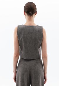 Grå herringbone ärmlös topp med en croppad bakdesign, med en mjuk textur och bred axelöppning.
