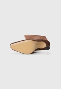 Brown suede high-heeled shoe featuring a pointed toe, smooth leather sole, and a black rubber accent on the heel's bottom edge.