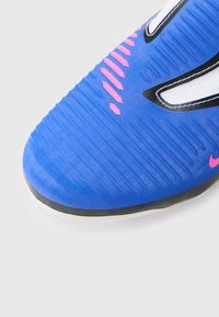 Μπλε ποδοσφαιρικό παπούτσι με υφασμάτινο συνθετικό πάνω μέρος, τονισμένο με ροζ γραμμές, μαύρες λεπτομέρειες και λεία, στρογγυλεμένη μύτη.