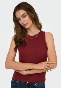 Tops en maille sans manches bourgogne avec un col rond, ourlet côtelé et tissu texturé. Associé à un jean en denim foncé.