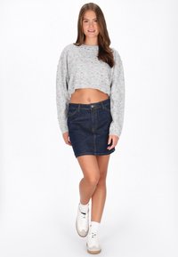 Grijze cropped sweater met kleurrijke spikkels, gecombineerd met een mini-rok van donker denim. Witte sneakers en enkelsokken maken de outfit compleet.